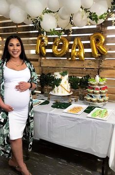 a pregnant woman standing in front of a table with desserts and balloons on it