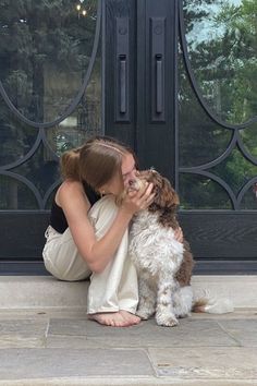 a woman is kissing her dog on the front steps with an iron door in the background