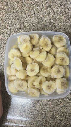 a plastic container filled with sliced bananas on top of a counter next to a person's hand