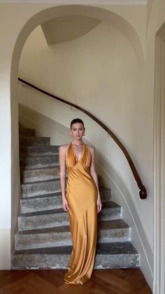 a woman standing in front of a staircase wearing an orange dress and gold shoes with her hands on her hips