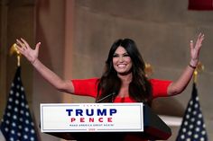 a woman standing at a podium with her arms up in the air and one hand raised