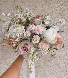 a bouquet of flowers is being held by someone's hand in front of a wall