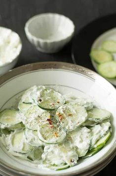 cucumber salad in a white bowl on a black table with other dishes around it