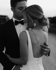 a man in a tuxedo and a woman in a white dress are standing close to each other