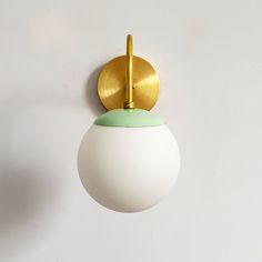 a white and green light hanging from a wall next to a gold plated hook