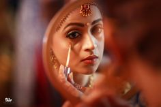 a woman is looking in the mirror while holding a brush and makeup powder to her face