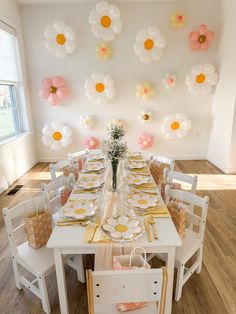 a dining room table set up with plates and flowers on the wall behind it,