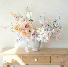 a vase filled with lots of flowers sitting on top of a wooden table next to a white wall