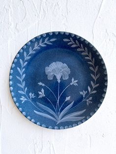 a blue plate with white flowers on it hanging from the side of a wall,