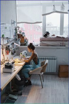 a woman sitting at a table in front of a sewing machine on top of a wooden floor