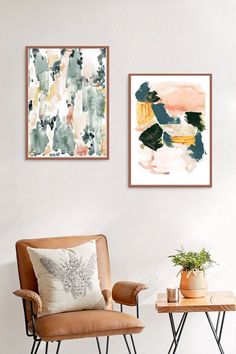 two framed paintings hang on the wall next to a chair and table with a potted plant