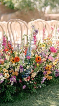 an arrangement of flowers lined up along the side of a row of white chairs at a wedding