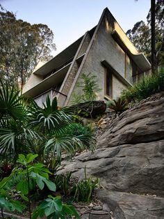 the house is built on top of a rock and surrounded by greenery, with large rocks surrounding it