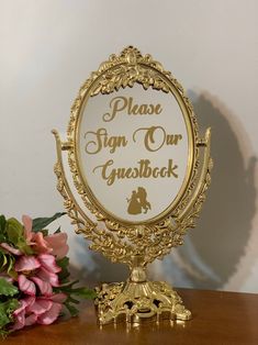 there is a sign on the table that says please sign our guestbook and flowers