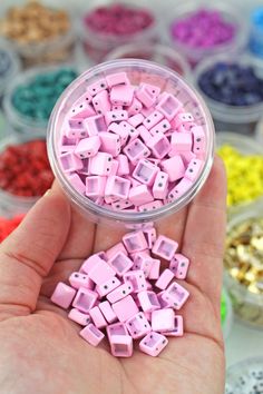 a hand holding a small container filled with pink and blue plastic beads next to many other colored buttons