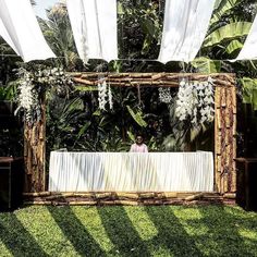 a person sitting at a table in the middle of some grass with white drapes over it