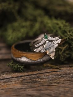 two wedding rings with green and white stones on top of each other sitting on a piece of wood