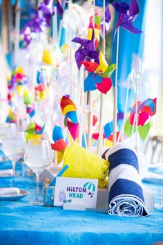 a blue table topped with lots of colorful pinwheels next to wine glasses and napkins