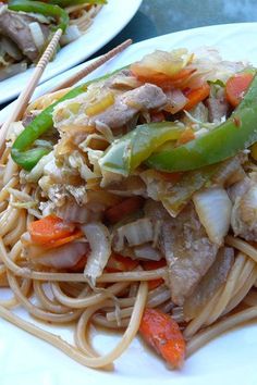 two plates with noodles, meat and vegetables on them next to chopsticks in the foreground