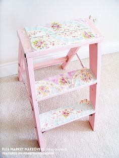 a pink wooden table with floral designs on the top and bottom shelf, in front of a white wall