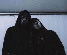 two men with painted faces and black hoodies on their face are standing in front of a white curtain