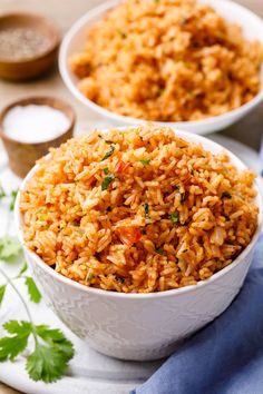 two white bowls filled with rice and garnished with parsley on the side