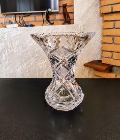 a clear glass vase sitting on top of a table next to a brick wall and television