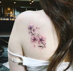 the back of a woman's shoulder with pink flowers on her left shoulder and purple petals on her right arm