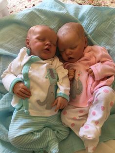 two baby dolls laying next to each other on a bed