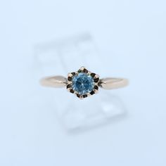 an engagement ring with a blue topazte surrounded by black diamonds on a white background