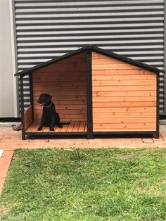 a black dog sitting in its kennel on top of the grass next to a building