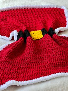 a crocheted red and white blanket laying on top of a bed next to a stuffed animal