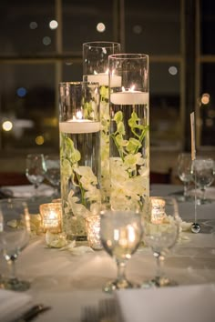 two tall vases filled with white flowers and lit candles on top of a table