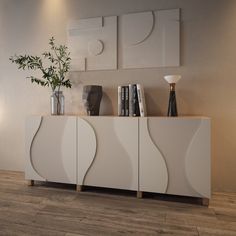 a white sideboard with vases and books on it next to a plant in a vase