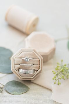 two wedding rings sitting on top of a ring box next to some spools of thread