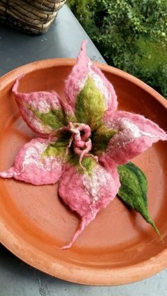 a pink and green flower is on an orange plate with some grass in the background