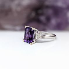 This Deep Purple Amethyst Ring is an elegant and timeless accessory crafted in solid 14k white gold. The emerald cut 10x8mm center stone is highlighted by sparkling baguette diamond accents. Perfect for February birthdays or to make a statement. Elegant Emerald Cut Purple Jewelry, Elegant Purple Emerald Cut Jewelry, Classic Amethyst Ring With Rectangular Stone For Formal Occasions, Elegant Rectangular Amethyst Ring For Formal Occasions, Elegant Emerald Cut Amethyst Promise Ring, Elegant Solitaire Amethyst Ring With Emerald Cut, Elegant Emerald Cut Amethyst Ring, Elegant Amethyst Ring With Rectangular Stone For Formal Occasion, Elegant Octagon Amethyst Ring For Formal Occasions