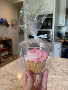 a person holding up a cupcake wrapped in plastic