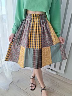 a woman standing in front of a window wearing a green sweater and skirt with multicolored squares on it