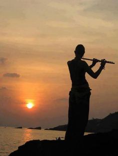 a man playing the flute in silhouette at sunset