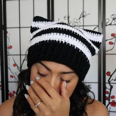 a woman covers her face with her hands while wearing a black and white cat hat