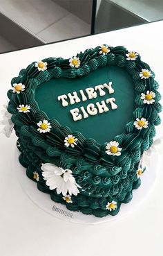 a green heart shaped cake with white daisies and the words thirty eight on it