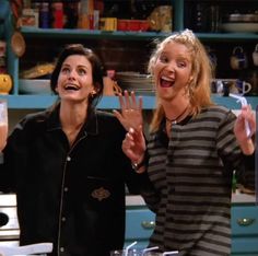 two women standing in a kitchen with one holding her hands up and the other smiling