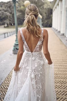 a woman in a wedding dress walking down the street with her back to the camera