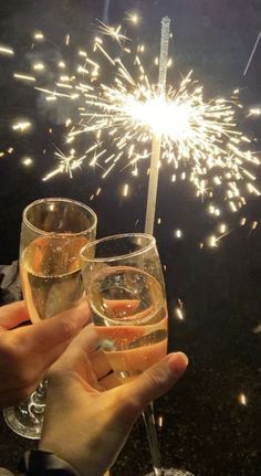 two people holding champagne glasses with sparklers in the background