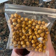 a hand holding a plastic bag filled with chickpeas on top of a counter