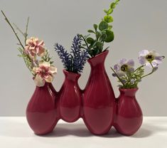 three red vases with flowers and greenery in them sitting on a table top