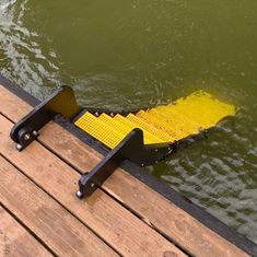 a yellow caution sign sitting on top of a wooden dock next to the water's edge