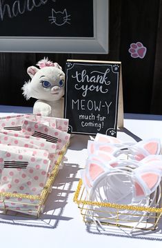 a table topped with lots of paper bags and stuffed animals next to a sign that says thank you meowy much for coming