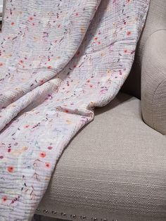 a cat laying on top of a couch next to a white chair with a blanket over it